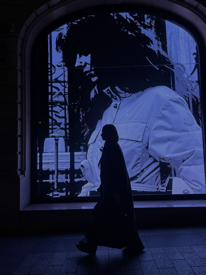 Kielo walking past a lit shop window at night, in silhouette